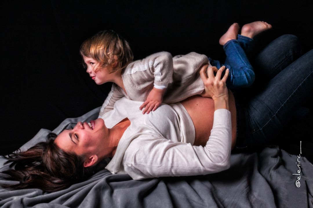 fotos del embarazo con hijos. fotografia de mamá embarzada en estudio en Mollet del Vallès jugando en el suelo con su hija
