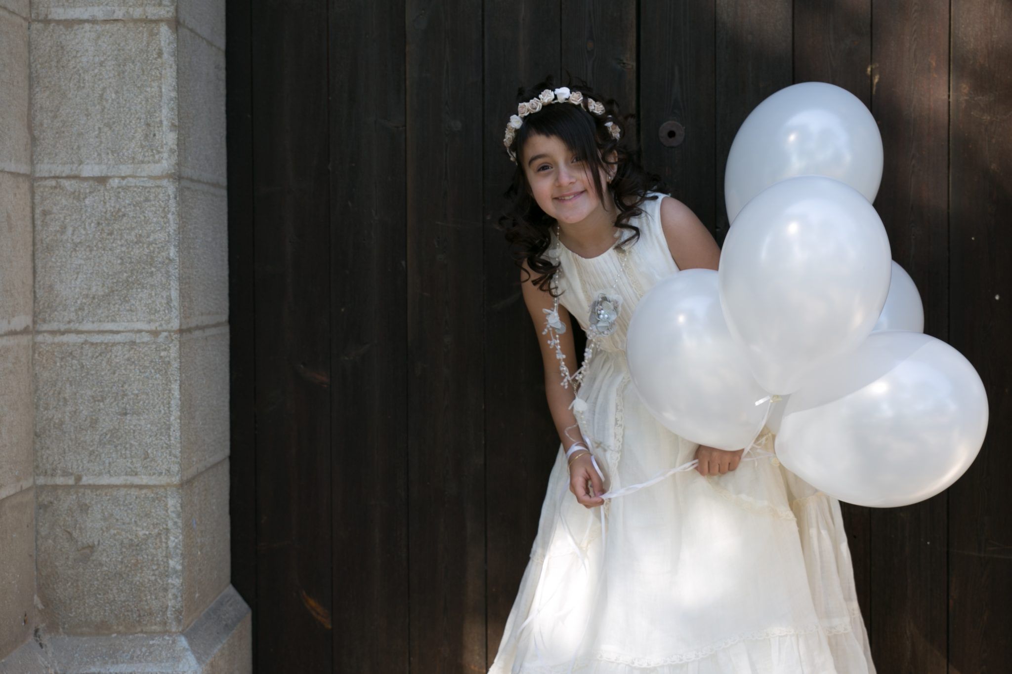 niña con vestido de comunión sosteniendo globos blancos en sesión exterior