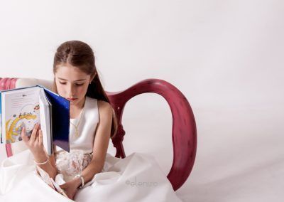 Laia vestida de comunión lee un libro. reportaje de comunión de laia en estudio de elenircfotografia. Elena Rubio, elenirc fotografía infantil en Mollet