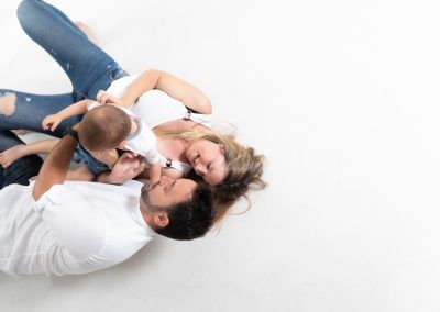 Familia tumbada en el suelo con su bebé durante una sesión fotográfica en casa, imagen natural y cotidiana