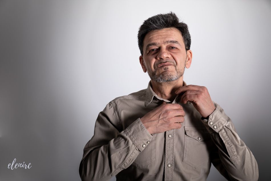 Retrato en estudio de un hombre ajustándose la camisa, centrado en el gesto y la expresión