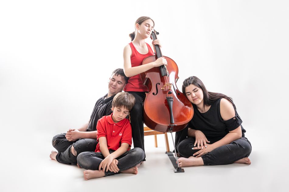 Primos de diferentes edades con violonchelo en estudio | Mollet del Vallès Primos de edades infantil, adolescente y joven creando una fotografía artística en estudio mientras una de ellas toca el violonchelo y los demás juegan a dormir, como recuerdo para su abuela