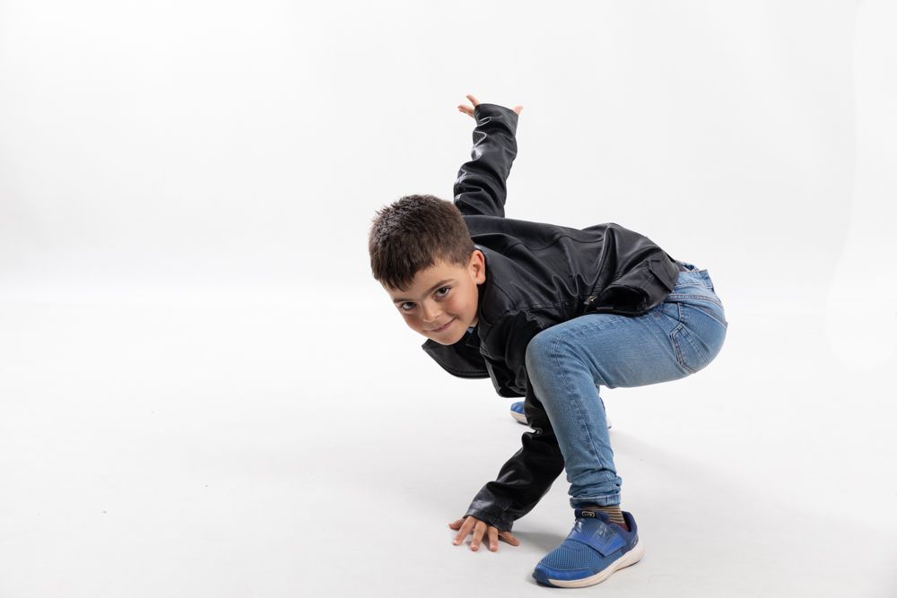Fotografia infantil en Mollet del Vallès · Cómo trabajar la empatía en los niños. Fotografía de estudio de un niño moreno con cazadora negra feliz jugando a tocar el suelo. elenirc fotografia Elena Rubio fotógrafa infantil Barcelona