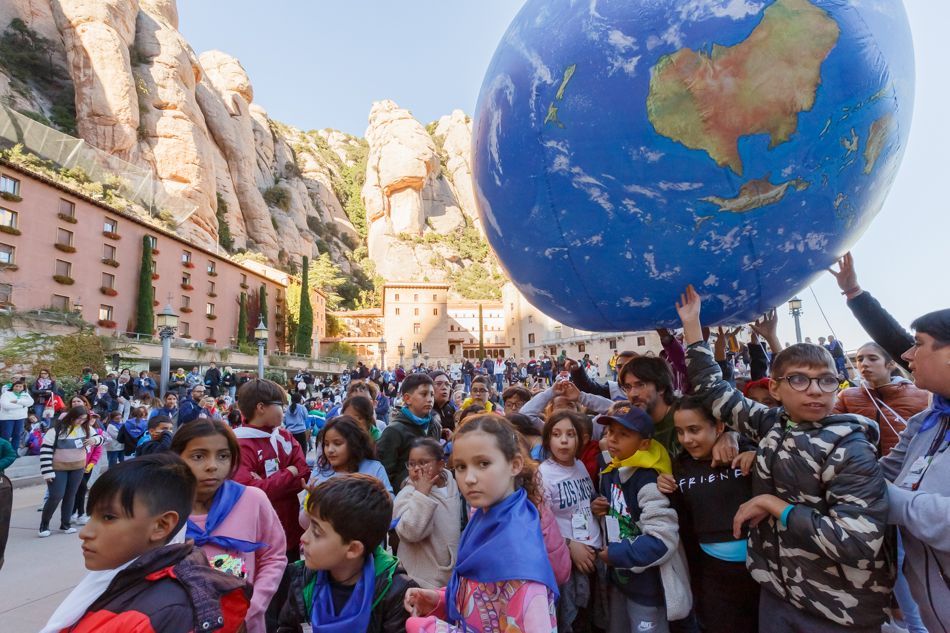 Niños y niñas participando en un evento cultural al aire libre, con una gran esfera del planeta Tierra, convocado por cristianos sin fronteras en el entorno de Montserrat.