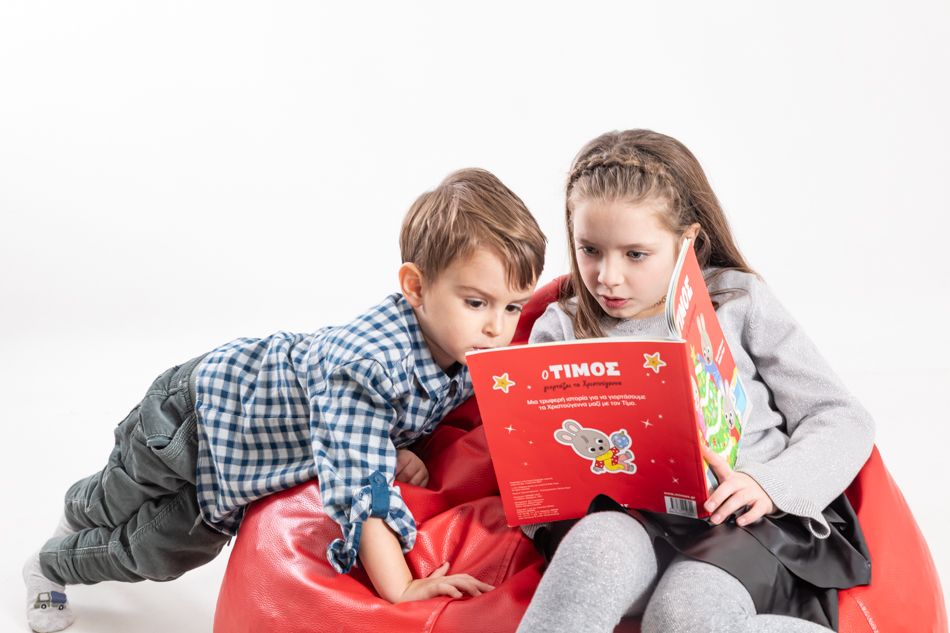 prima enseñando un libro infantil en griego a su primo durante una sesión de fotos familiar en Mollet del Vallès
