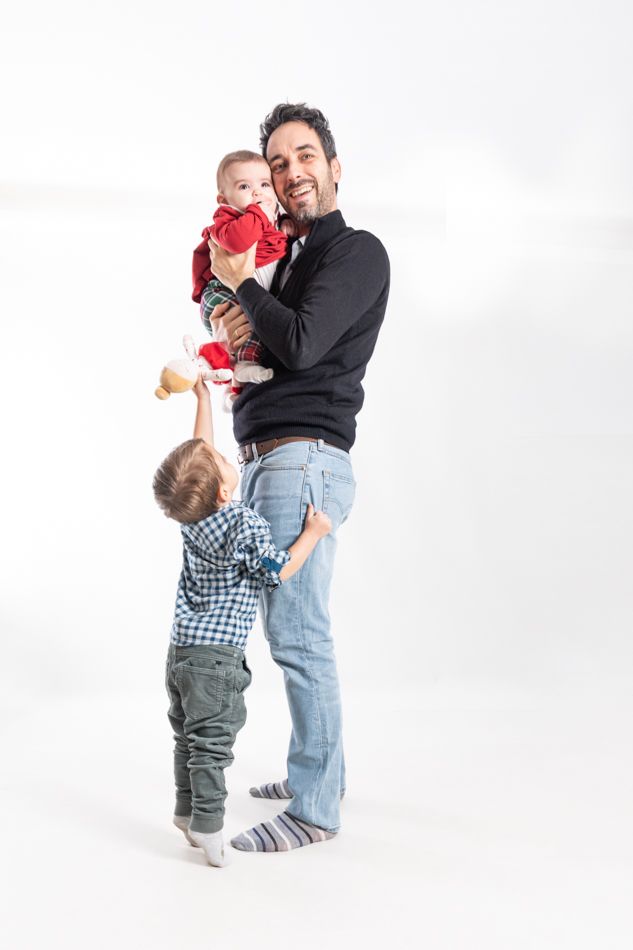 20241228- elenirc-185151 Padre sosteniendo a su bebé mientras su hijo mayor se acerca, fotografía de familia centrada en el vínculo y la relación entre hermanos
