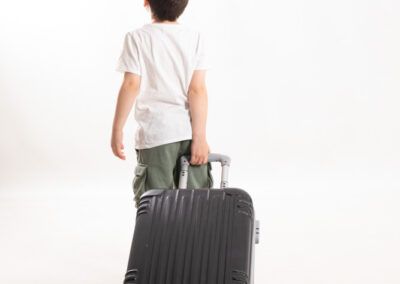 Foto de niño de espaldas que lleva decidido una maleta.Fotografia infantil y de familia Benvinguts bessons