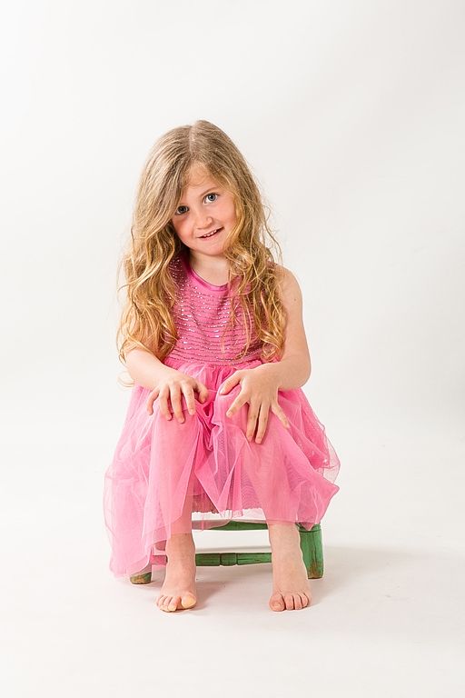 Imagen editorial de moda infantil, niña sentada en estudio con vestido rosa