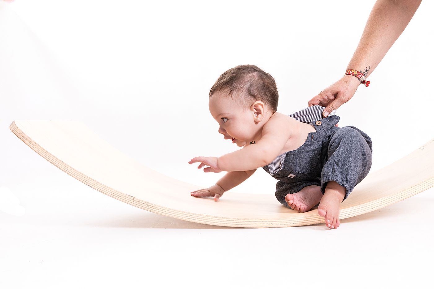 Bebé explorando el movimiento sobre una tabla de madera durante una sesión de fotografía en estudio, con una mano adulta evitando que se escape gateando