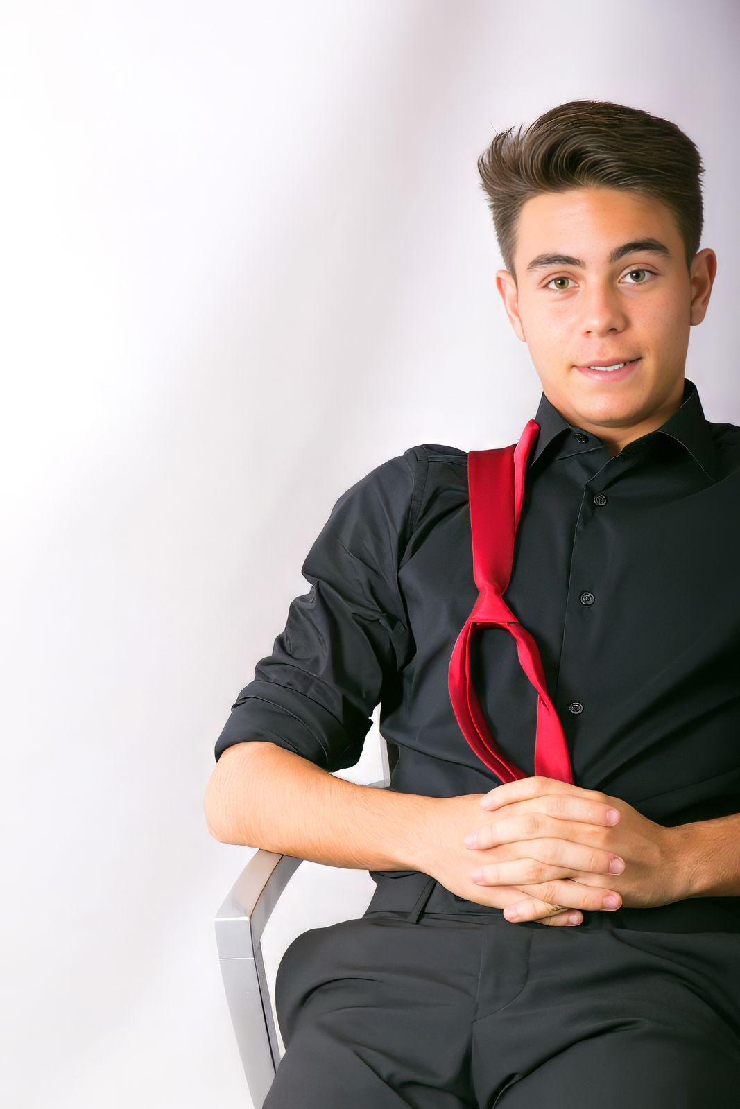 Adolescente vestido con camisa negra y corbata roja durante una sesión de retrato de graduación en estudio en Mollet del Vallès, por Elenirc Fotografia.