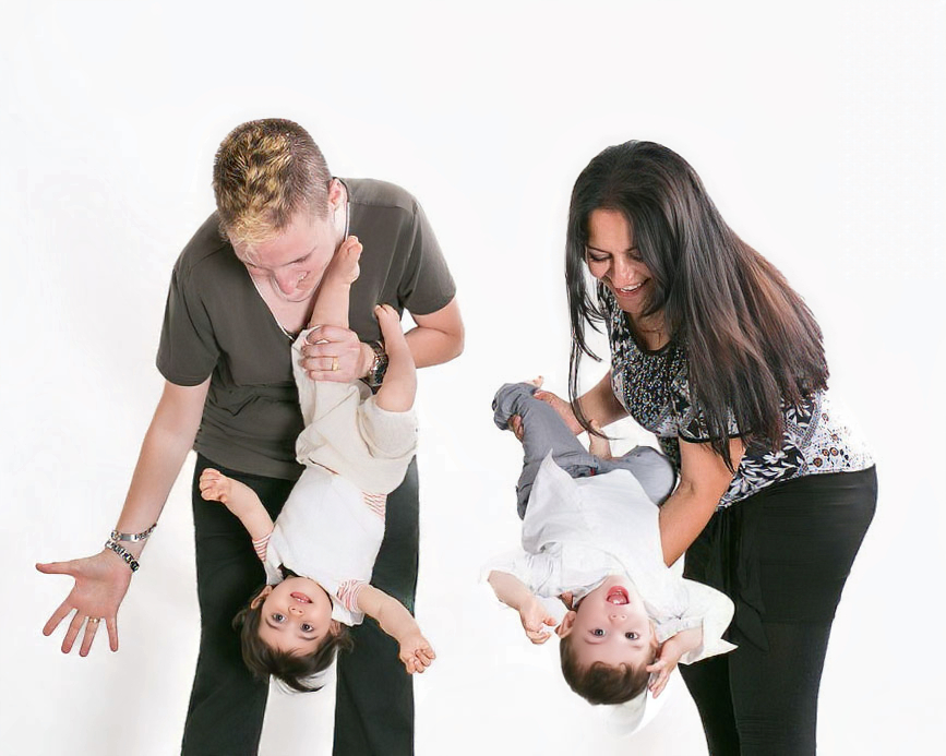 Mamá y mami juegan con sus gemelos durante una sesión de fotografía familiar en estudio, en un momento espontáneo y lleno de movimiento.