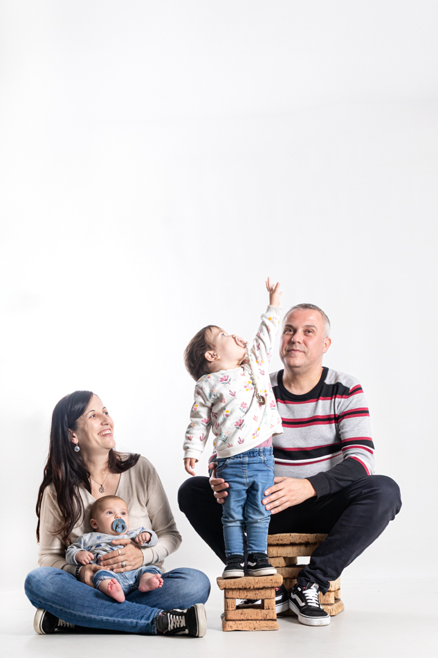 Madre y padre con su bebé y su hija mayor durante una sesión de seguimiento del bebé en estudio en Mollet del Vallès, viendo cómo crece la familia, por Elenirc Fotografia.