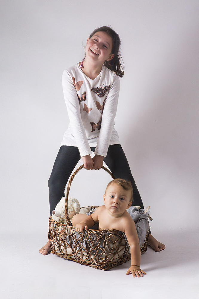 niña mayor junto a bebé en cesta en estudio