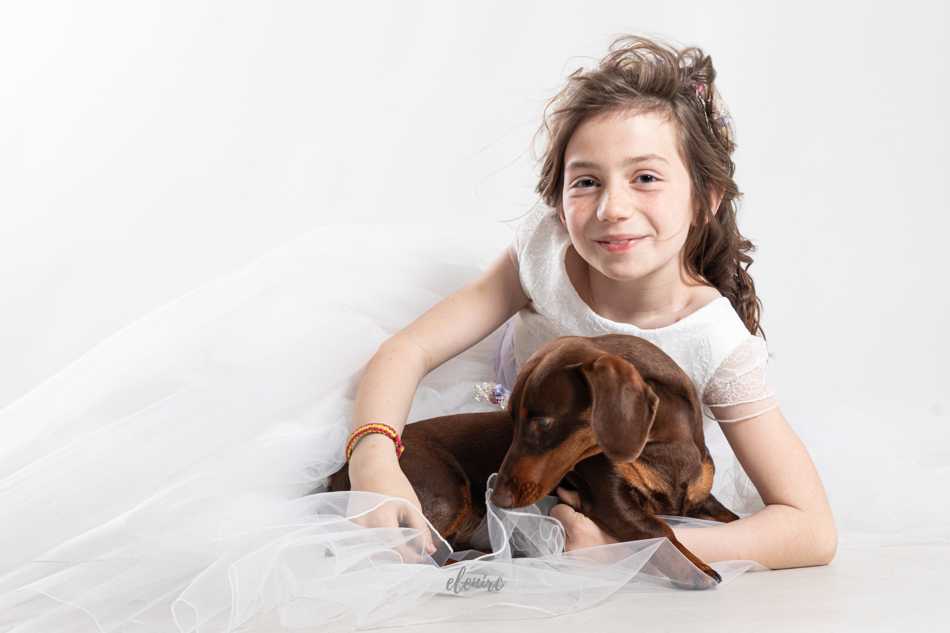 sesion de comunion en estudio niña contenta con su perro recostado elenirc