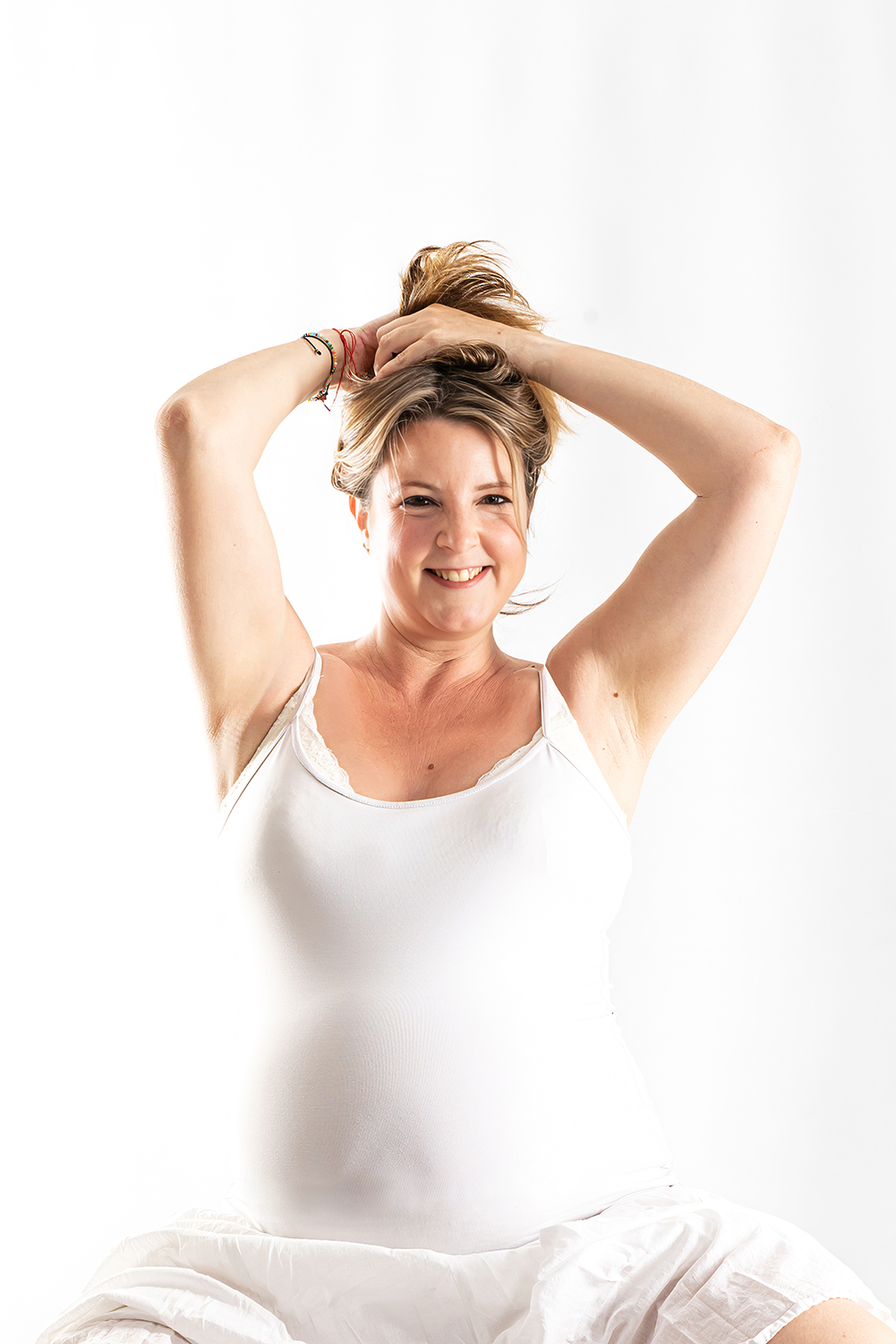 Mujer embarazada sonriendo mientras se recoge el cabello durante una sesión de fotografía de embarazo en estudio en Mollet del Vallès, por Elenirc Fotografia.