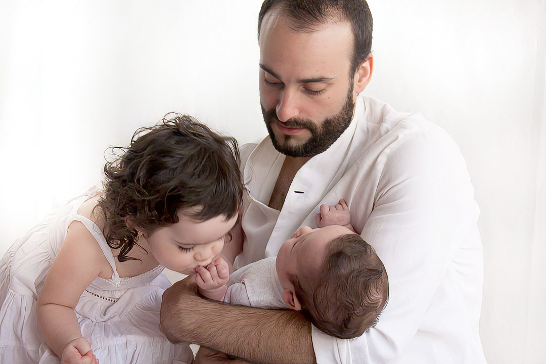 Los primeros días juntos Fotografía infantil a los dos meses y a los 2 años Niña besa hermanito en brazos de pap´por Elena Rubio para elenircfotografia