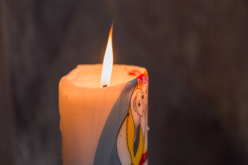 Luz, emoción y recuerdos compartidos Primer plano de un cirio bautismal encendido durante una ceremonia religiosa, por Elenirc Fotografia.