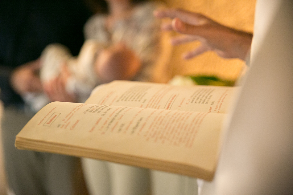Un rito lleno de significado Detalle de las manos de un párroco sosteniendo el libro del ritual abierto durante una ceremonia de bautizo en Barcelona, por Elenirc Fotografia.