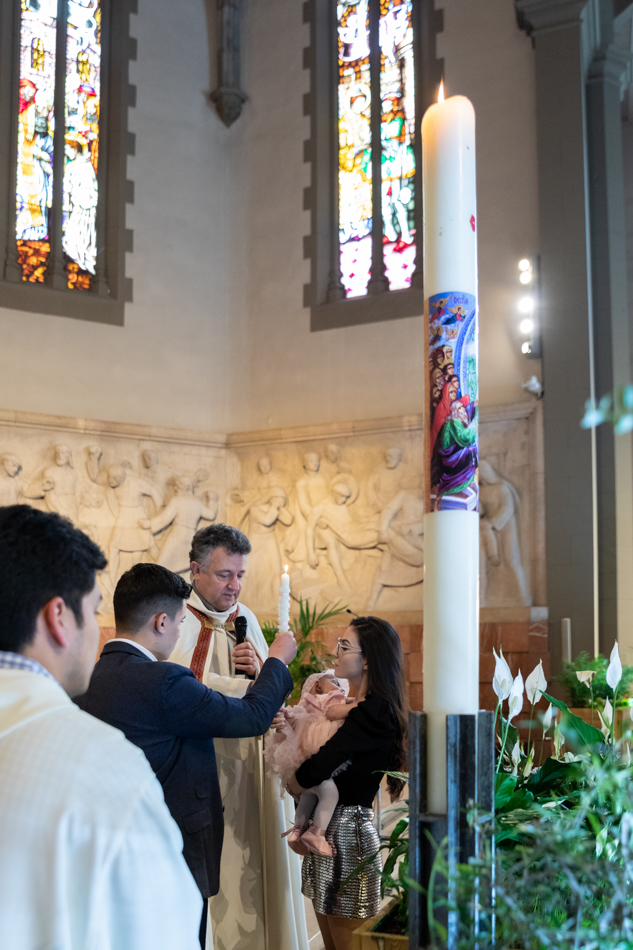 La entrega de la luz Momento del rito de la luz con los padrinos encendiendo la vela desde el Cirio Pascual en la Parroquia de Sant Esteve de Granollers, por Elenirc Fotografia.