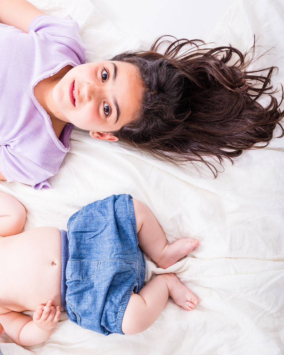 Niña con su hermanito en sesión de fotos de estudio en Mollet Fotografia de familia en estudio elenirc fotografia niña con su hermano bebé tumbados del revés durante una sesión de fotos divertida