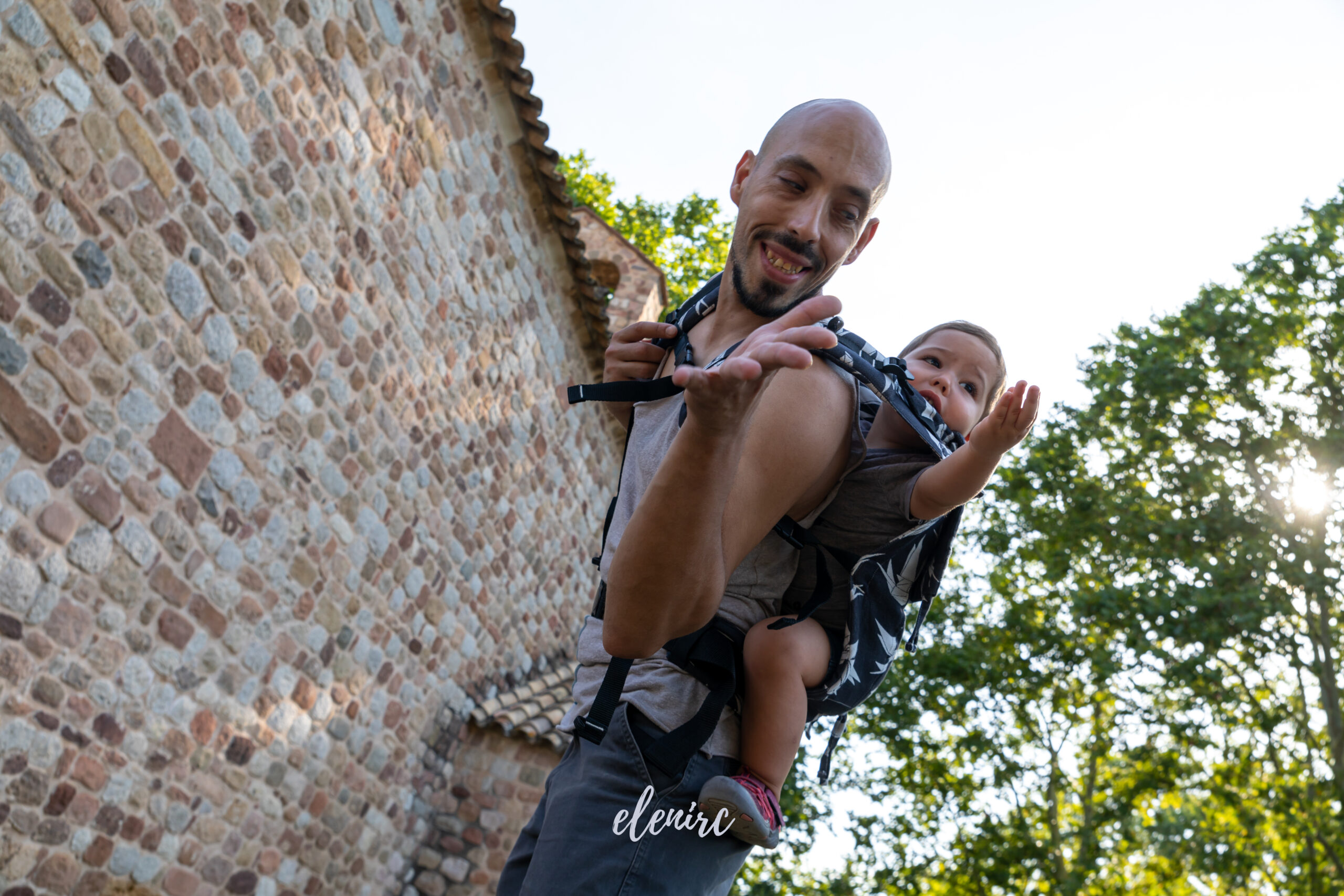 Fotografía comercial de porteo y crianza · Elena Rubio Retrato de un padre sonriendo con su bebé en una mochila portabebés a la espalda. Fotografía para un proyecto de crianza de Elena Rubio.