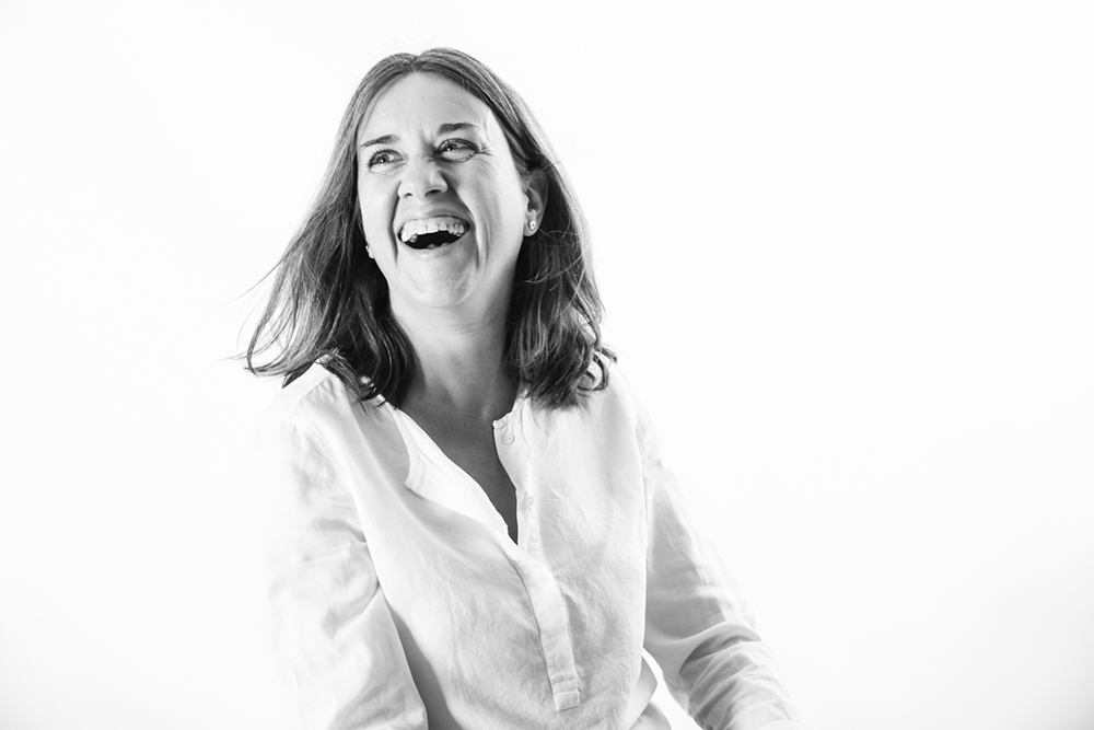 ALT: Retrato de una profesional riendo espontáneamente durante una sesión de fotos para su página web, en estudio y blanco y negro, por Elena Rubio · Elenirc Fotografia.