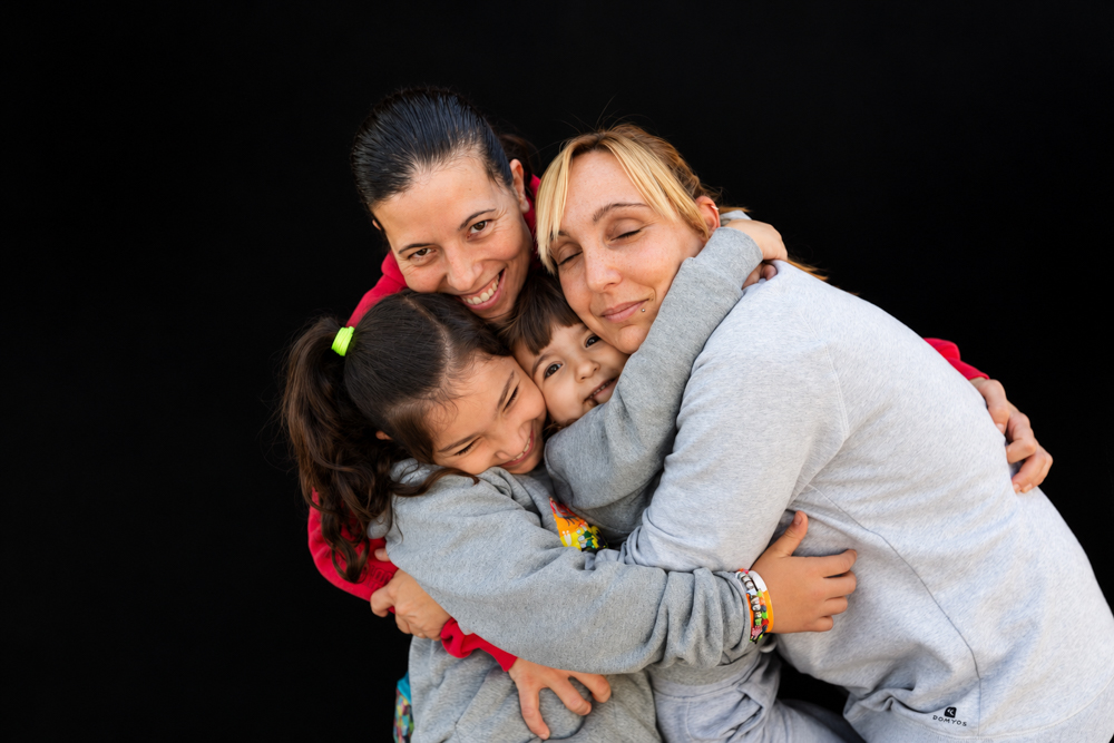 Dos mamás con su hija compartiendo un momento de juego y sonrisas durante la Castañada de FLG · Famílies LGTBI+. Retrato de familia homoparental de Elena Rubio · elenirc.