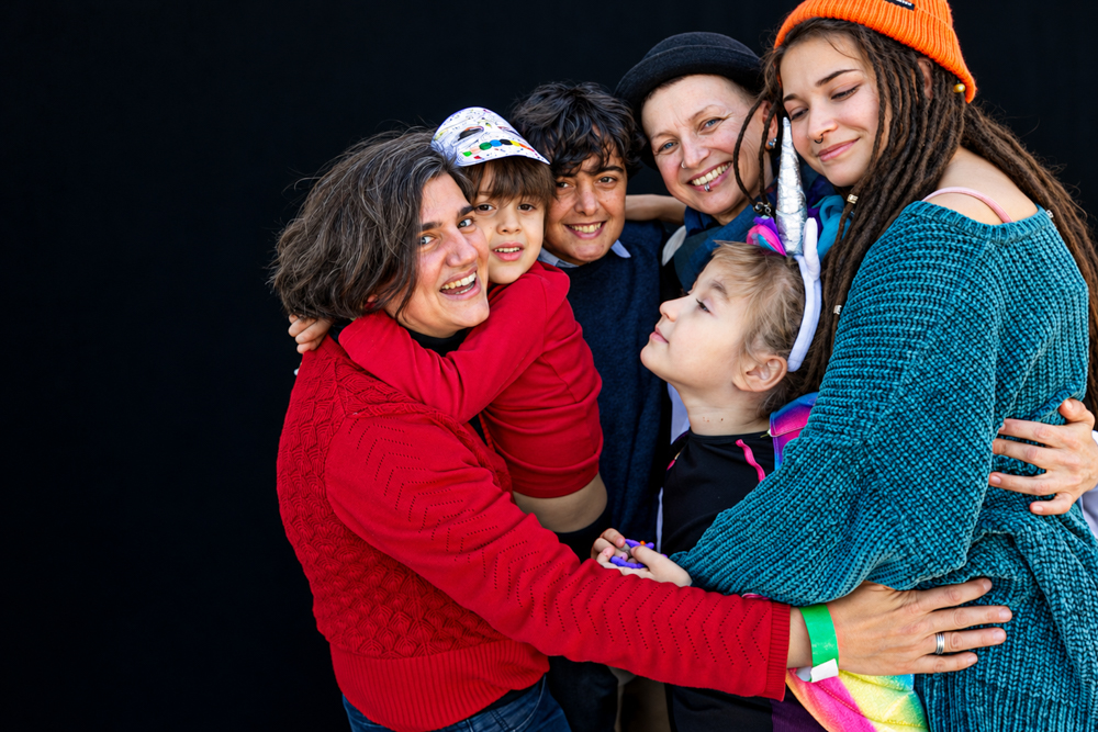 Familia con sus hijos y amigos compartiendo un abrazo colectivo Famílies LGTBI+. Retrato de diversidad familiar de Elena Rubio · elenirc.