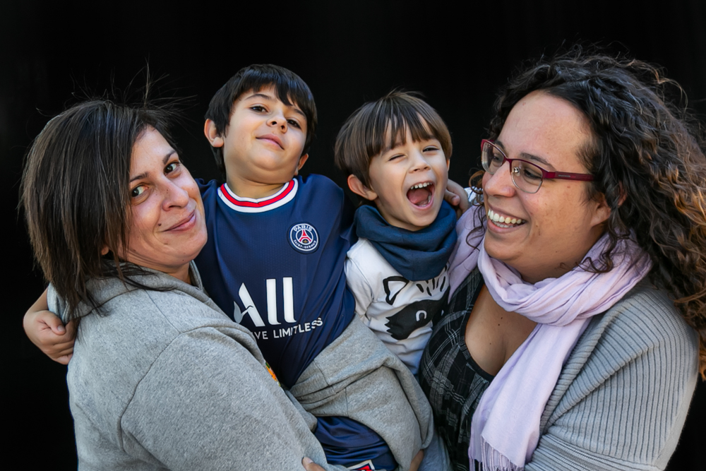 Dos mamás abrazan a sus dos hijos, que sonríen y ríen durante la Castañada de FLG · Famílies LGTBI+. Retrato de familia homoparental de Elena Rubio · elenirc.