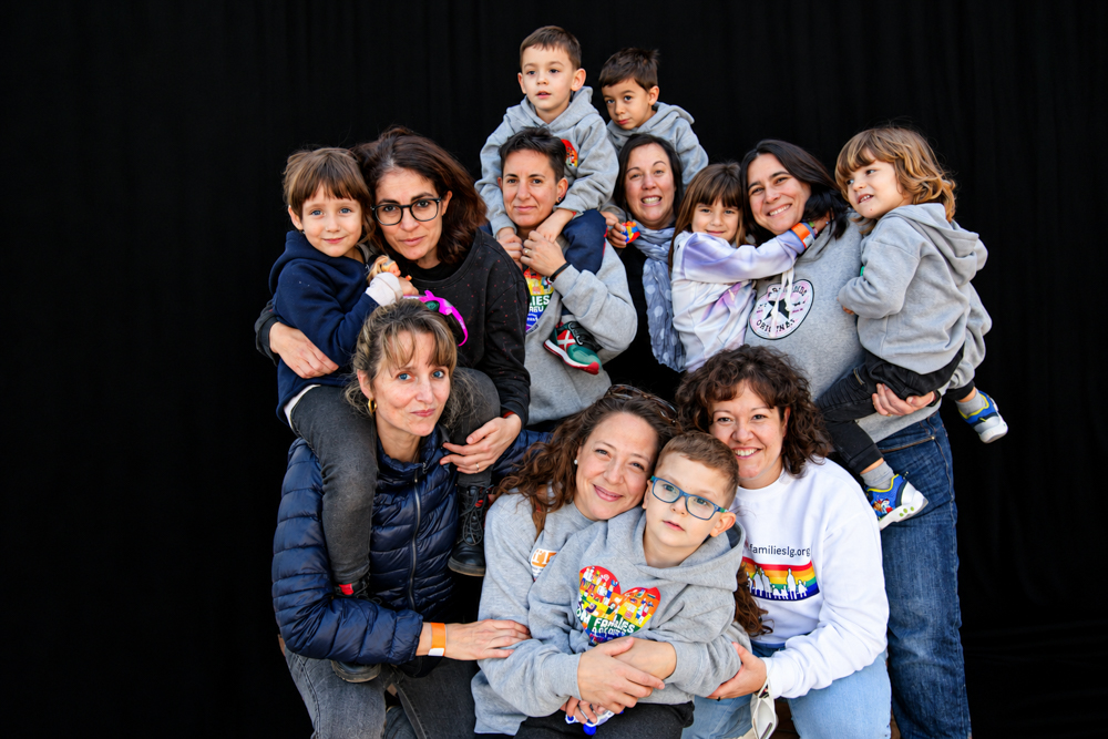 Familias diversas con sus hijos e hijas posando juntas y abrazadas ante un fondo negro durante la Castañada de FLG. Fotografía de Elena Rubio · elenirc.
