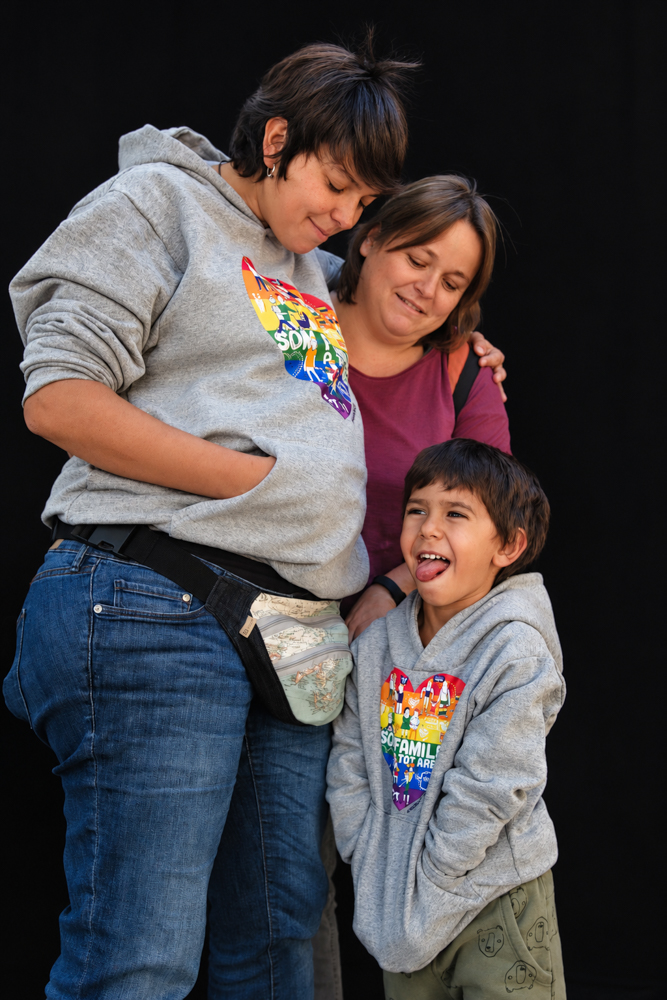 Familias LGTBI+ con sus hijos e hijas y una mamá embarazada, compartiendo un abrazo colectivo durante la Castañada de FLG. Fotografía de Elena Rubio · elenirc.