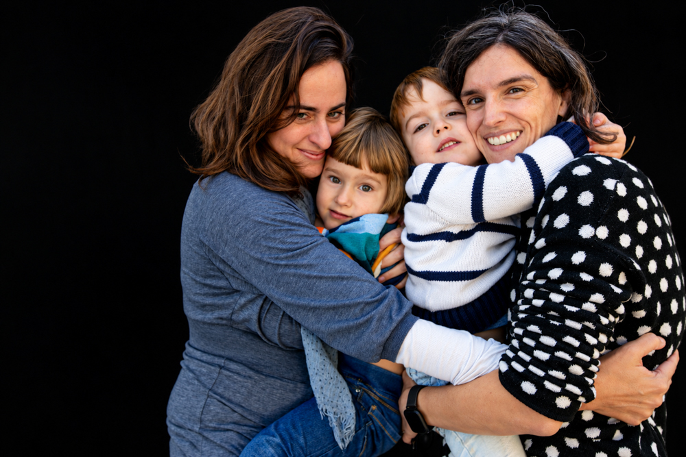 Dos mamás abrazan a sus dos hijos en un retrato de familia homoparental. Fotografia de diversidad familiar. Una colección de abrazos fotografiada por Elena Rubio · elenirc.