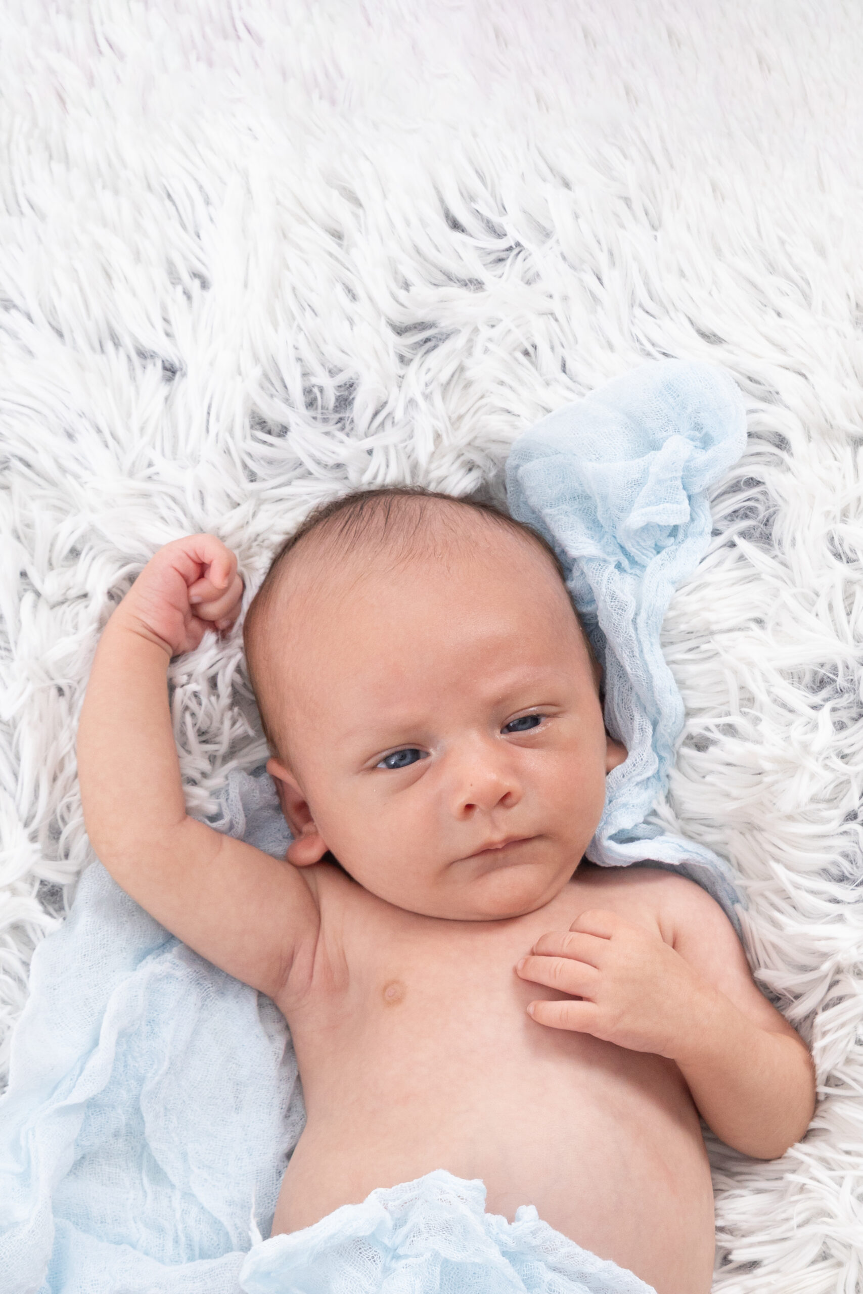 Fotografía newborn de bebé recién nacido despierto, con sus gestos y expresiones naturales, sobre una manta blanca con tejido azul. Elena Rubio.